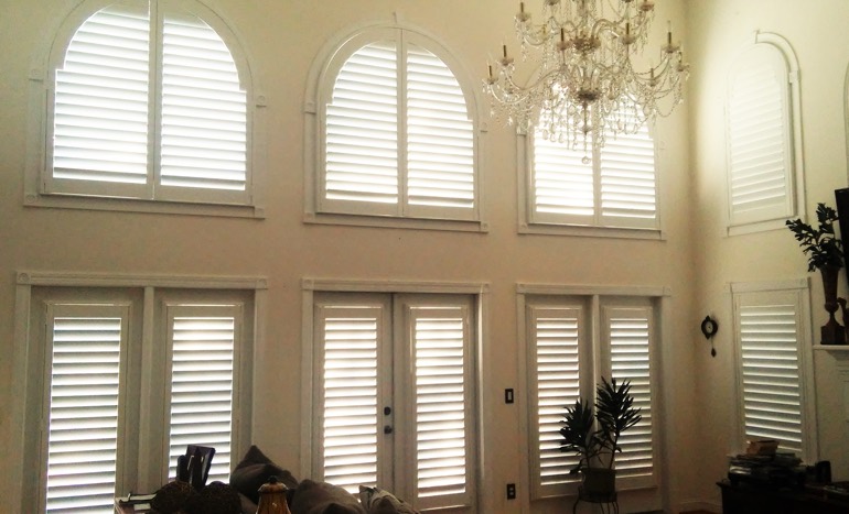 Entertainment room in open concept Honolulu house with plantation shutters on high ceiling windows.